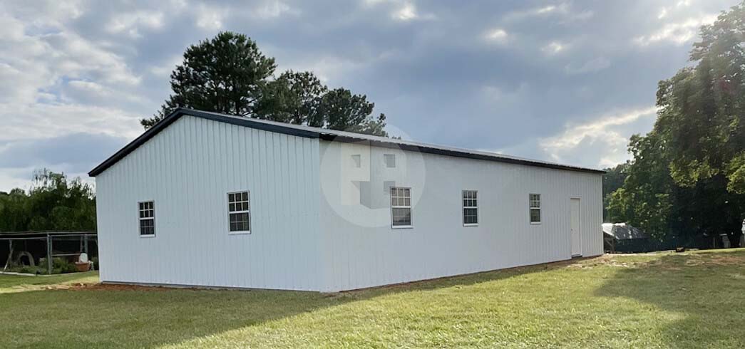 Long white metal utility building with a black roof, six windows along the side and a walk-in door at the end