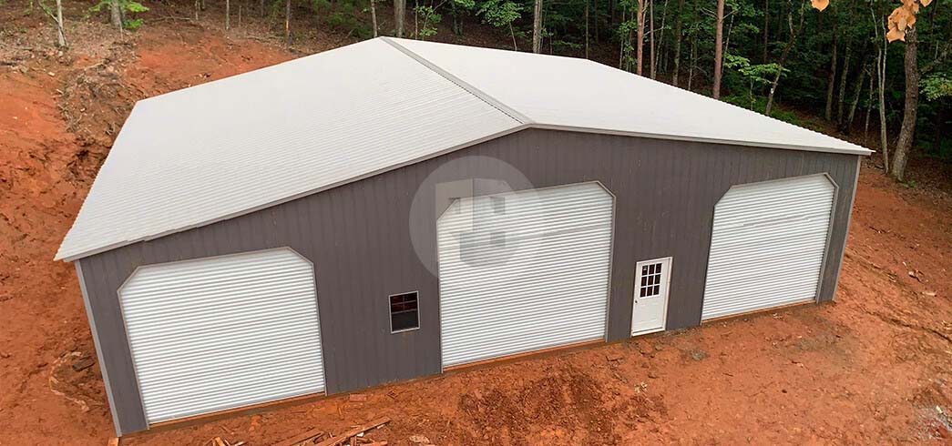 Three-bay grey metal garage with a white roof, roll-up doors across the front and a side walk-in door